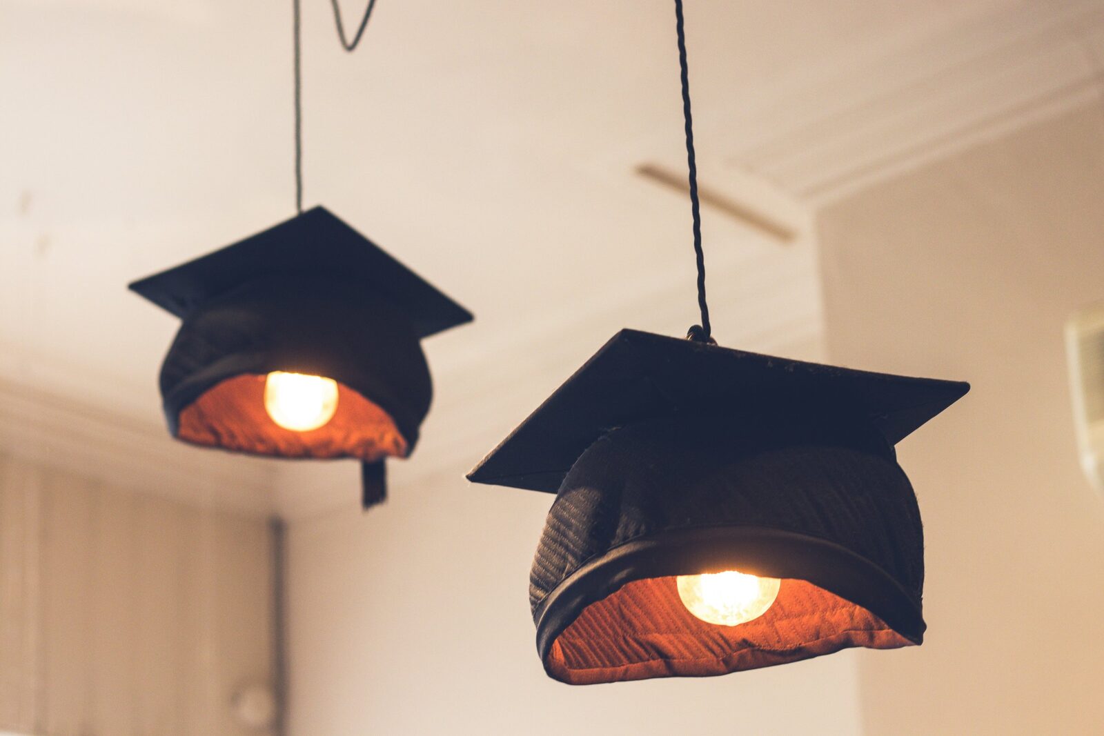Graduation caps hang from the ceiling, converted into pendant lights lit from within by lightbulbs.