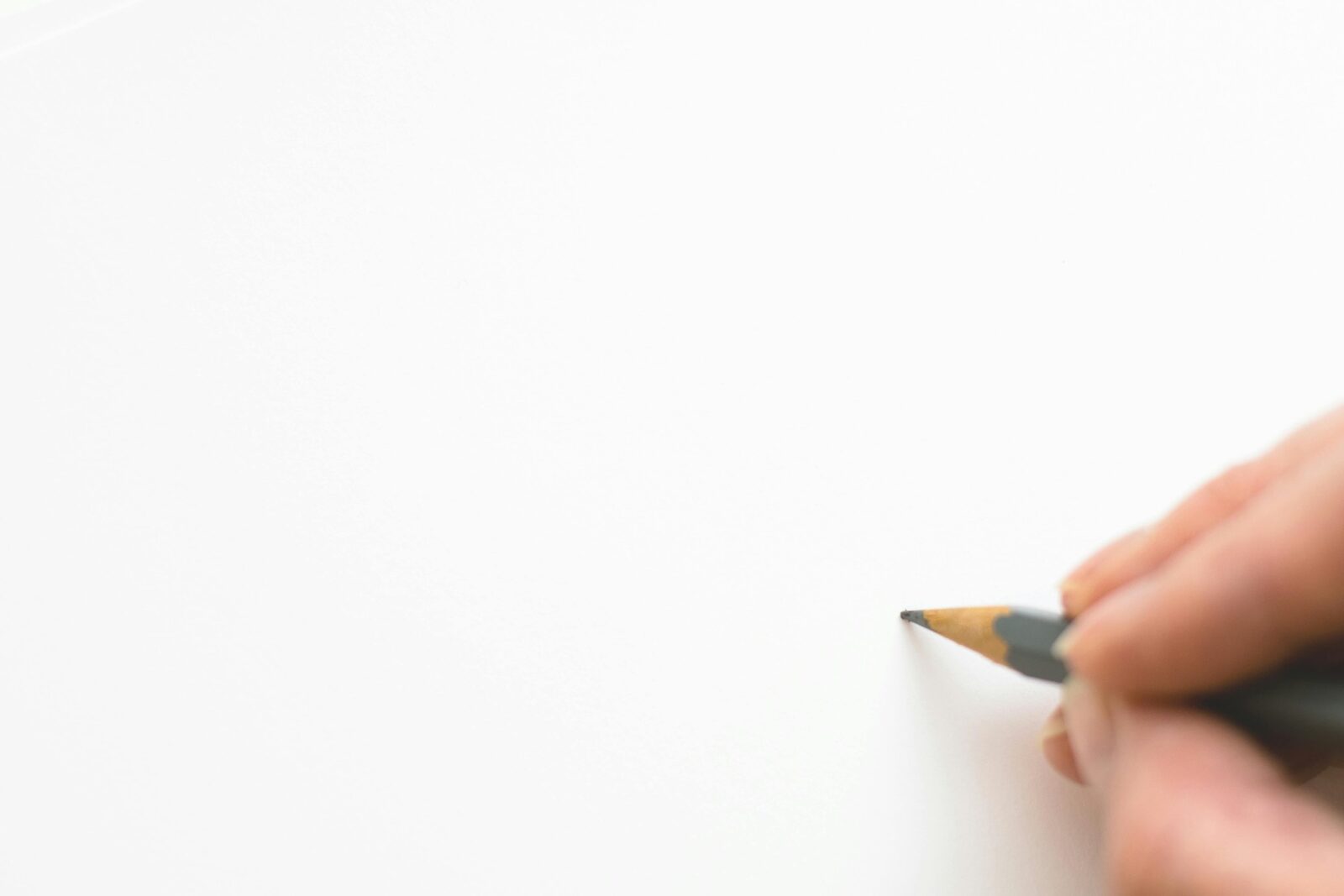 A minimalist image of mostly white space, with a hand holding a pencil about to begin writing.